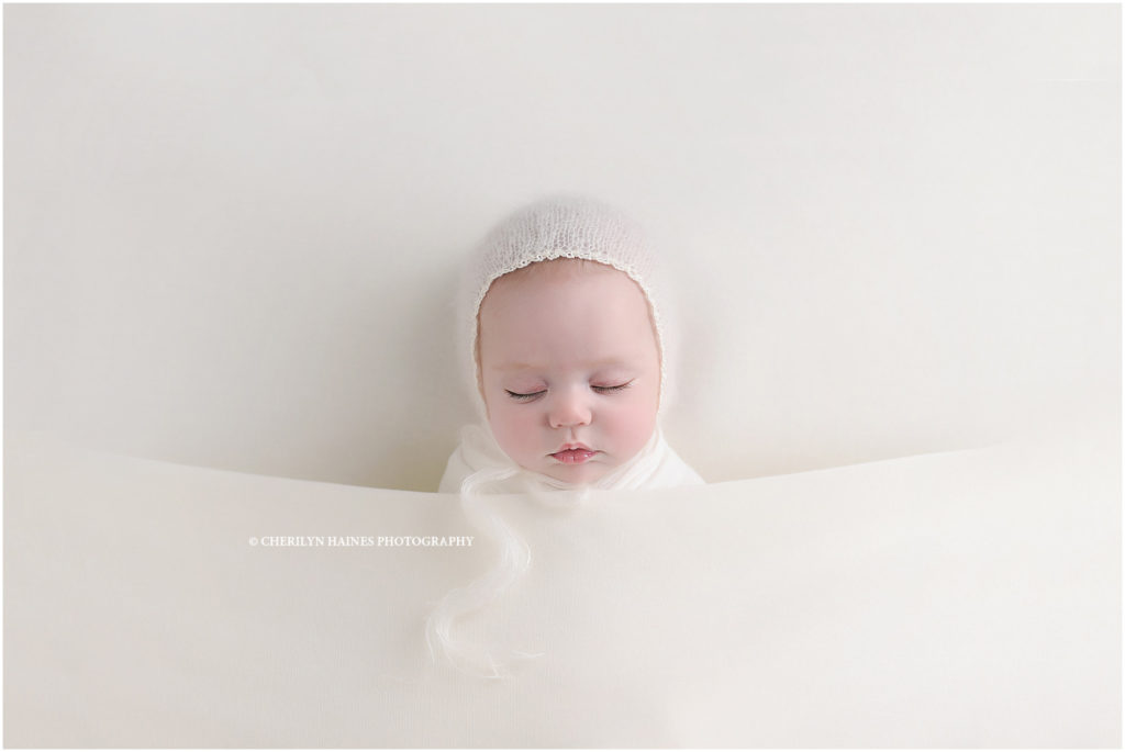 2 month old newborn baby girl photographed sleeping on white blanket with white bonnet