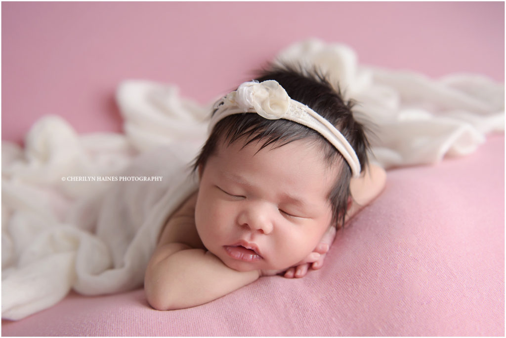 13 day old newborn baby girl photographed laying on pink fabric with white floral headband