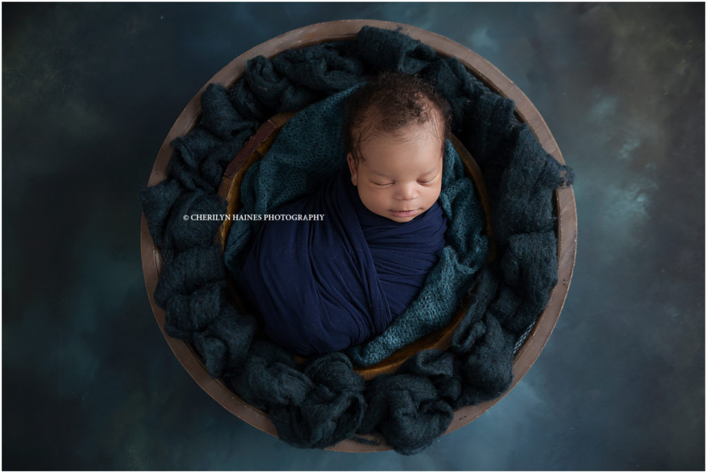 two week old newborn baby boy photographed swaddled in navy blue wrap, laying in basket with navy and teal backdrop; photograph by cherilyn haines photography