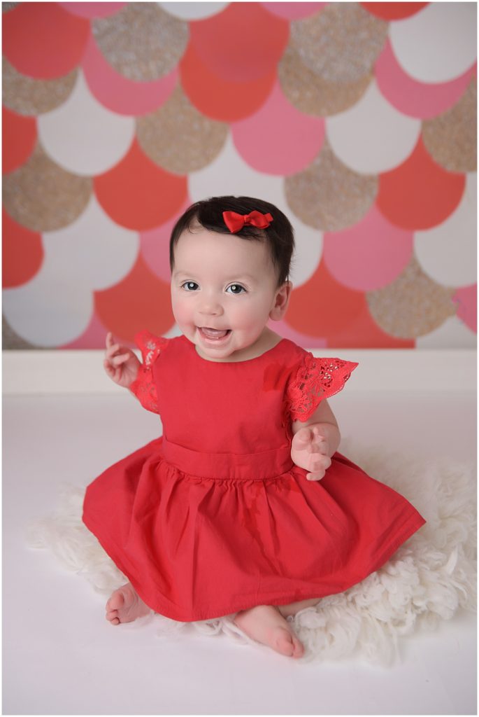 6 month old baby girl wearing red dress photographed on red, pink, and gold backdrop