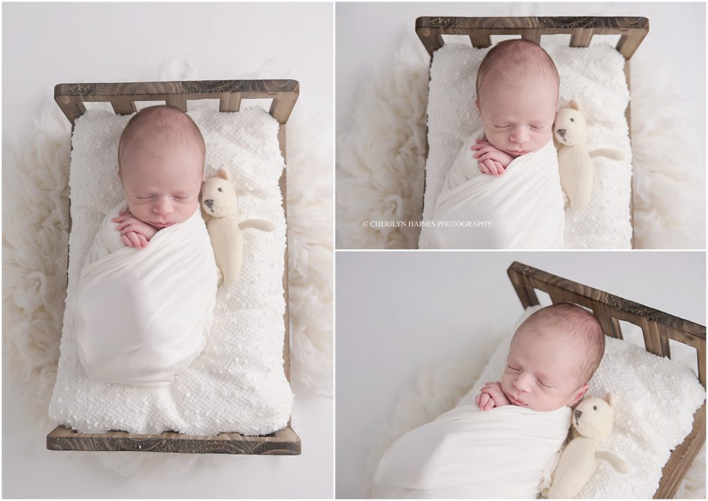 newborn baby boy photographed laying in wooden bed cuddling tiny teddy bear