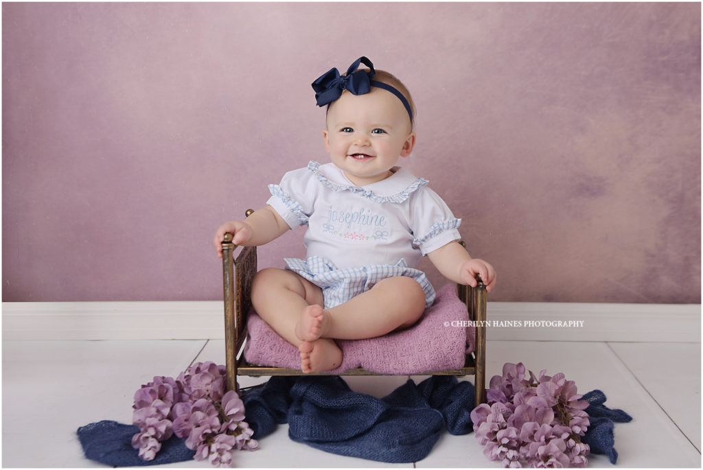 1 year old portraits of baby girl photographed sitting on antique brass baby bed with purple flowers