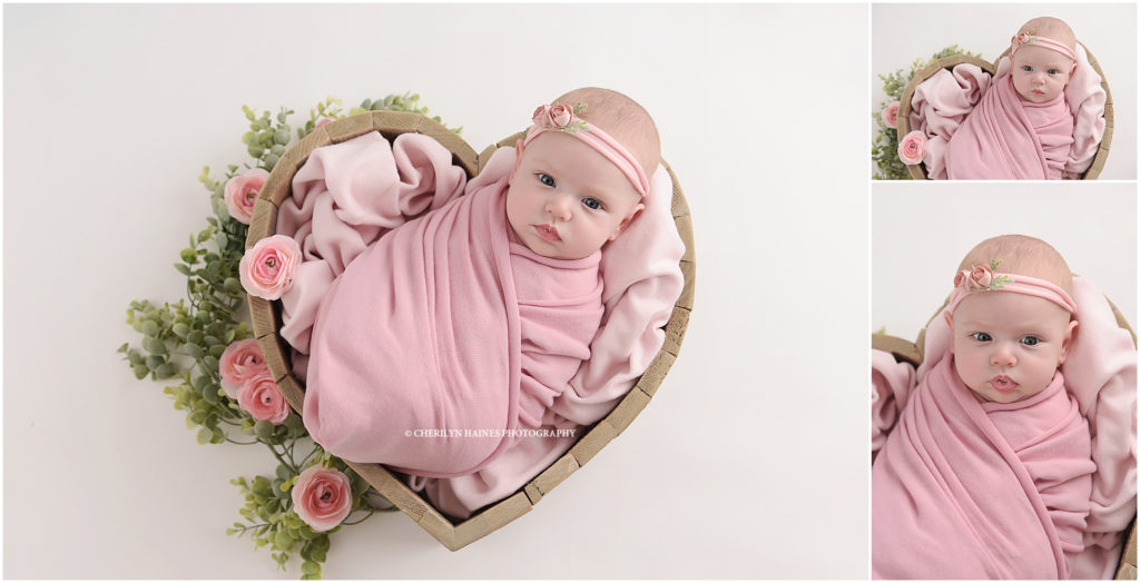 awake newborn baby girl posed in wooden heart prop with pink florals