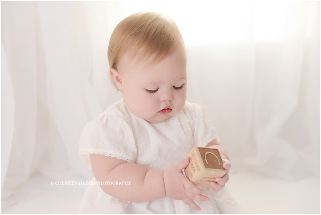 1 year old baby girl photographed in white dress sitting in front of window with white shears; photographed by cherilyn haines photography in louisiana