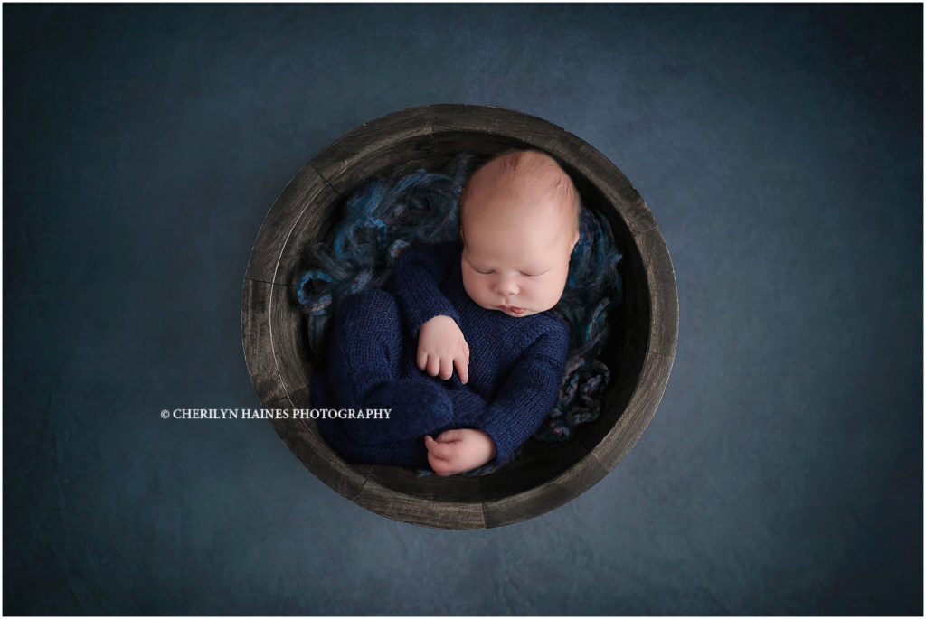 10 day old newborn baby boy photographed laying in dark gray wood bowl, wearing a navy crochet footed romper; photographed by cherilyn haines photography in baton rouge, louisiana