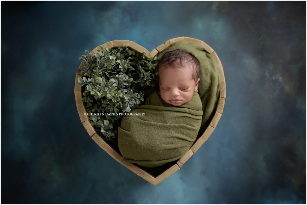2 week old newborn baby boy posed in heart shaped prop swaddled in green; photographed by cherilyn haines photography in louisiana