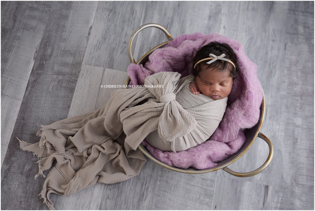 newborn portrait session in baton rouge, louisiana with cherilyn haines photography; 11 day old newborn baby girl photographed swaddled in gray bow wrap laying in bucket with purple blanket