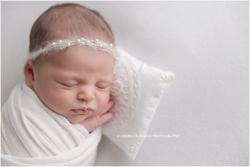 14 day old newborn baby girl photographed by cherilyn haines photography at studio in louisiana; baby swaddled in white with white headband laying on white crochet pillow