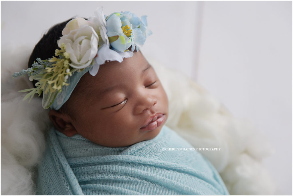 beautiful sleeping 11 day old newborn baby girl swaddled in light blue with a floral headband