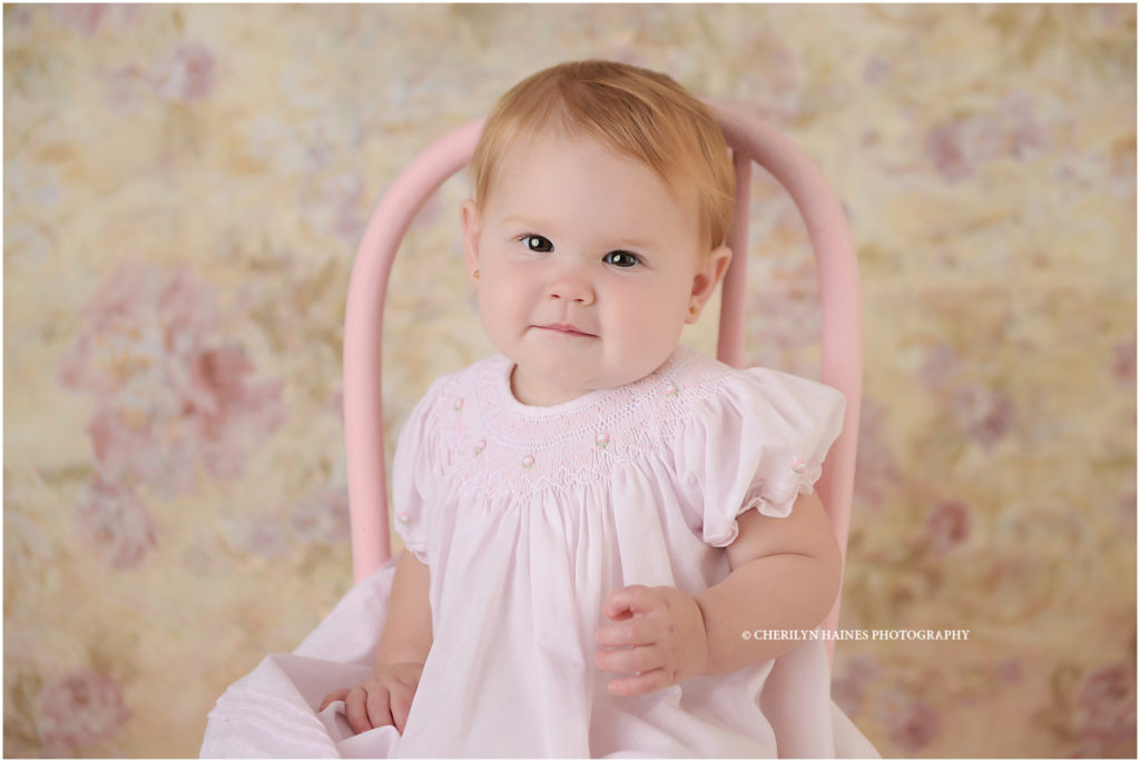1 year old baby girl photographed on pink stool with floral backdrop