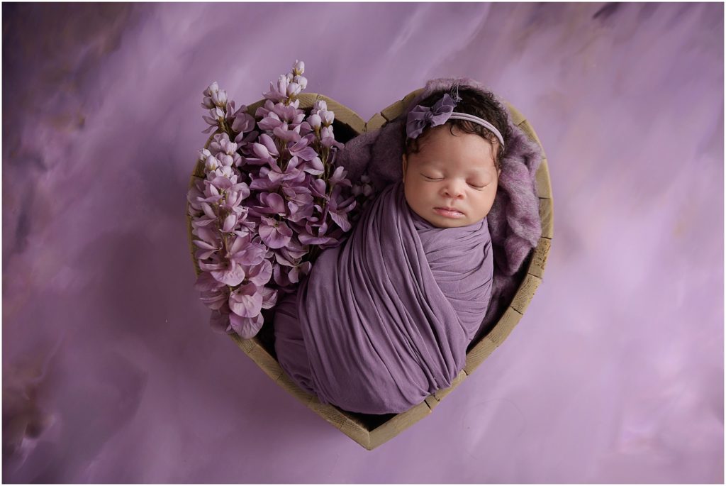 newborn baby girl photographed in heart shaped bowl with purple flowers; cherilyn haines photography