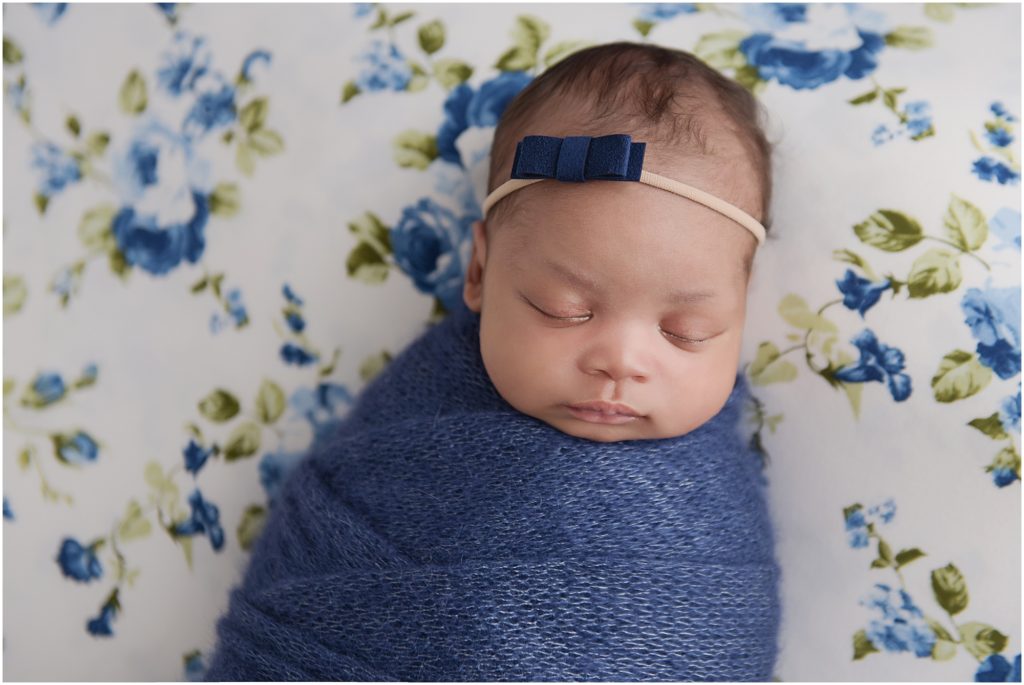 newborn baby girl photographed on blue and white floral blanket swaddled in dark blue