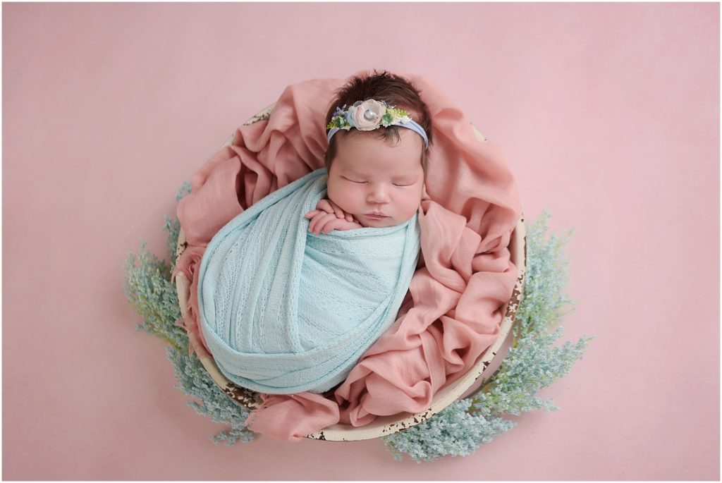 2 week old newborn baby girl photographed by cherilyn haines photography; baby girl swaddled in aqua wrap laying on bowl with pink blanket