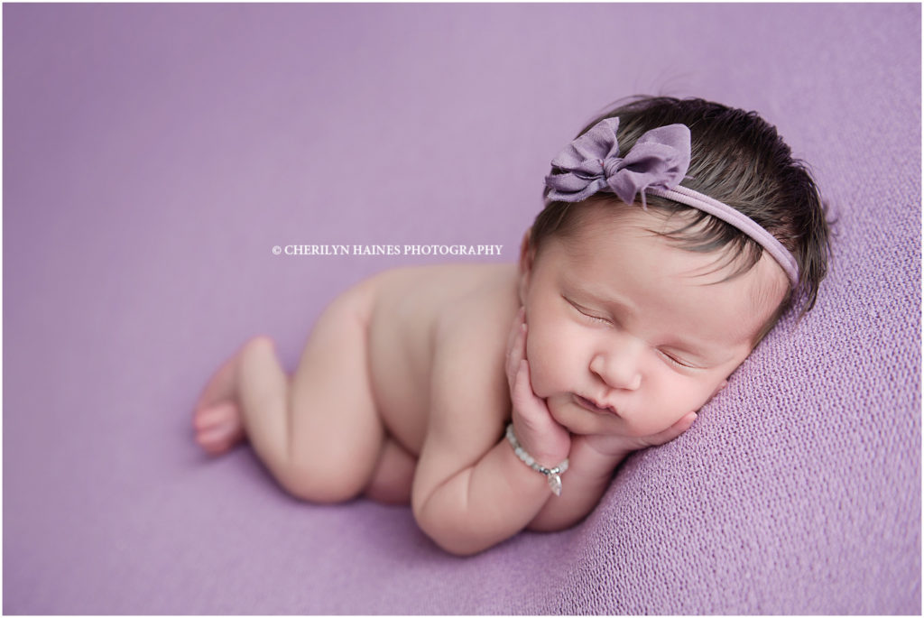 2 week old newborn baby girl photographed laying on purple blanket with purple bow; photography by cherilyn haines photography in denham springs, louisiana