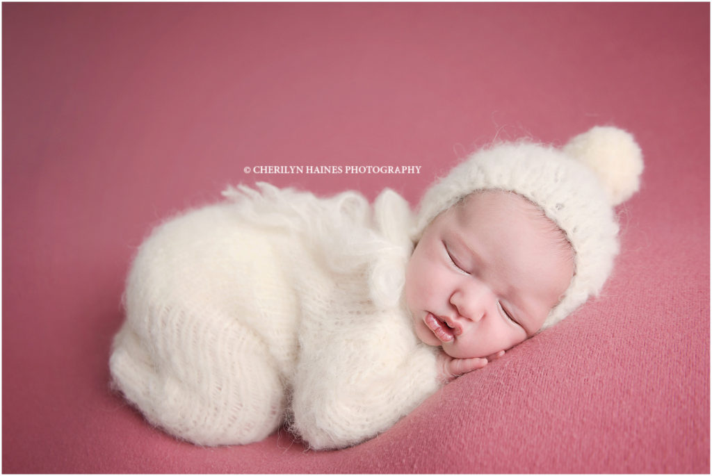 2 week old newborn baby girl photographed on rose pink blanket wearing a knit footed pajama and pom hat set