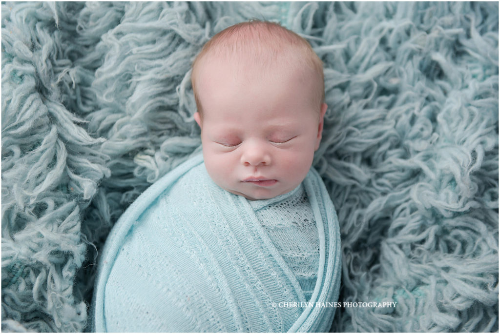 newborn baby boy photographed in baton rouge, louisiana by cherilyn haines photography; baby swaddled in light blue laying on light blue flokati rug