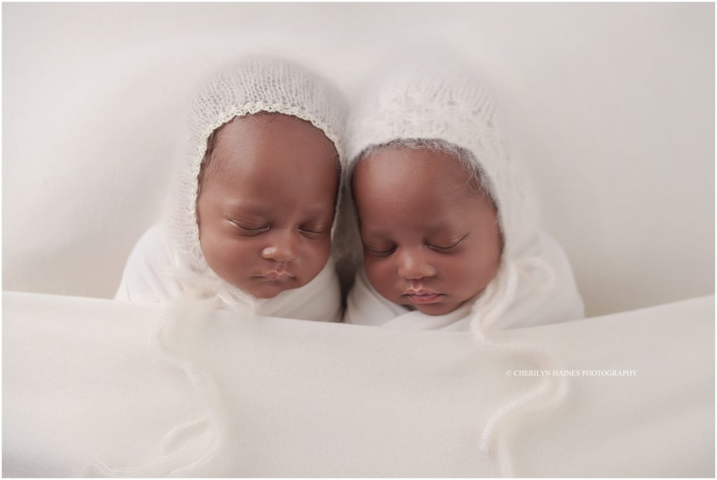 newborn twin girls wearing crocheted white bonnets