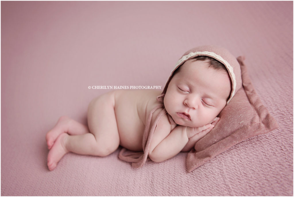 3 week old newborn baby girl photographed laying on pink blanket with matching rose colored pillow and bonnet; photography by cherilyn haines photography in louisiana