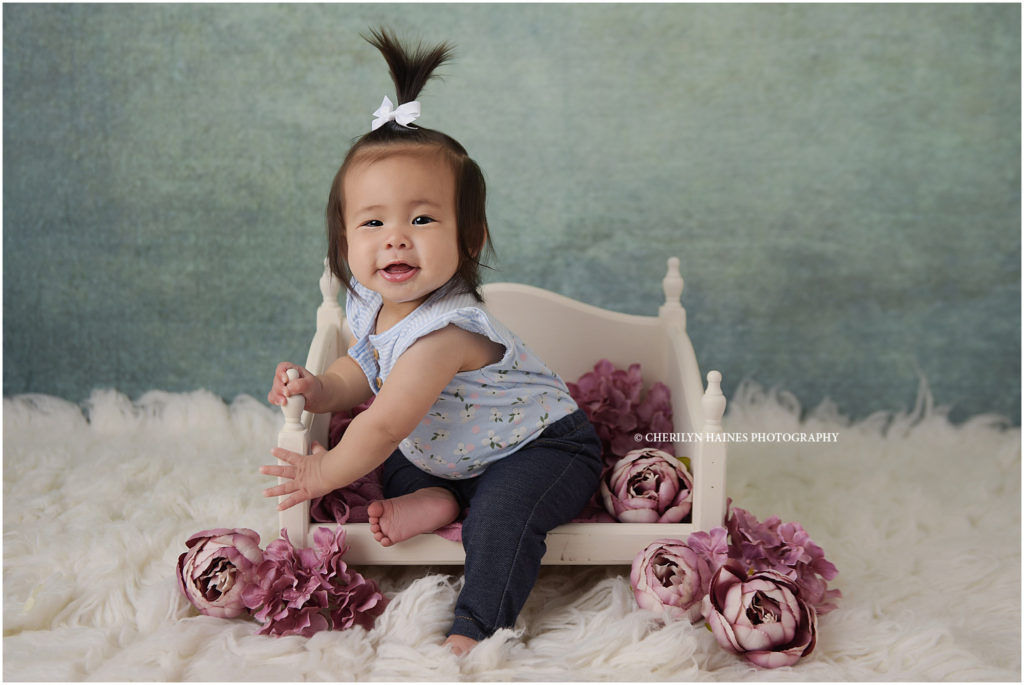 7 month old baby girl photographed on antique white bed with plum colored flowers