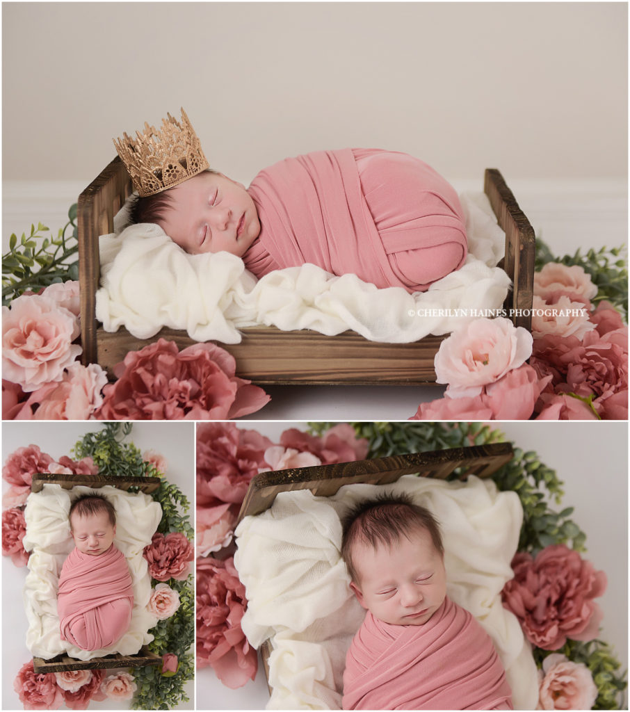 newborn baby girl photographed on brown bed with pink and mauve flowers and a gold tiara