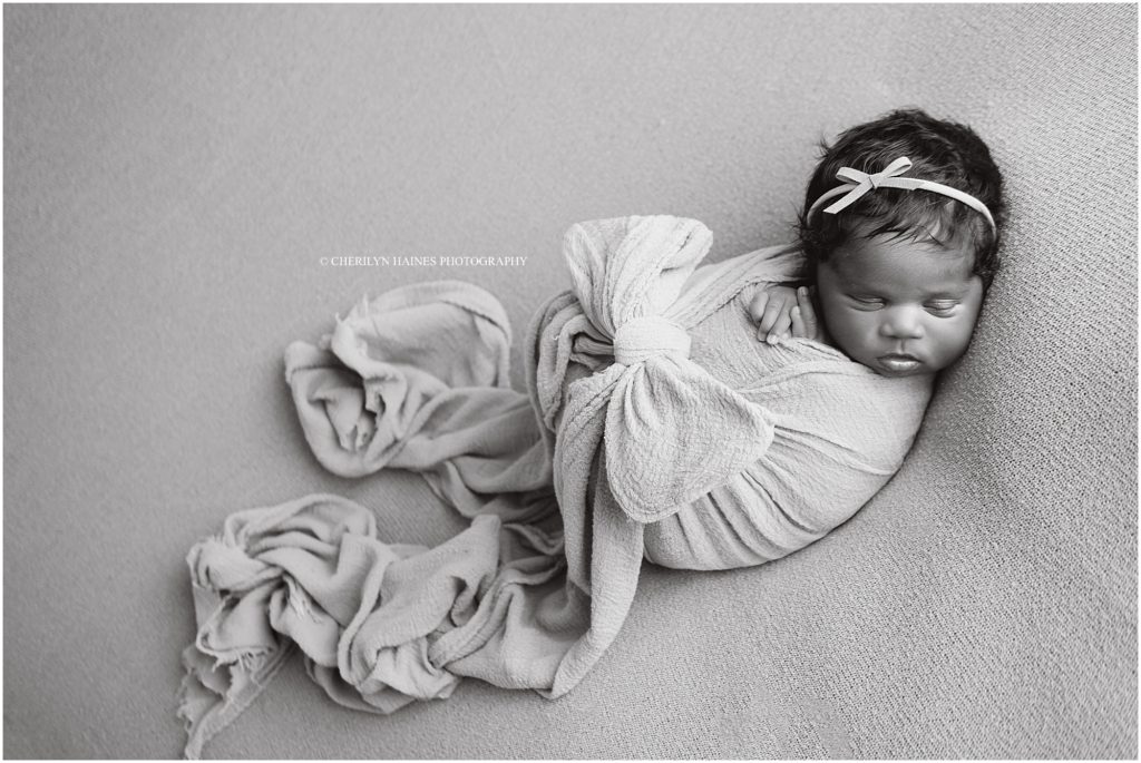 black and white newborn portrait with baby girl swaddled with a bow