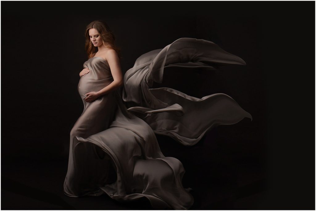 Baton Rouge, Louisiana Fine Art Maternity Photographer, Cherilyn Haines Photography; pregnant mom photographed wearing long silver flowing silk chiffon fabric with dramatic lighting. This session was photographed with a Nikon D750 and Sigma Art 50mm 1.8 lens. The lighting was an Einstein 640 with a 64: White PLM umbrella on Savage Seamless paper