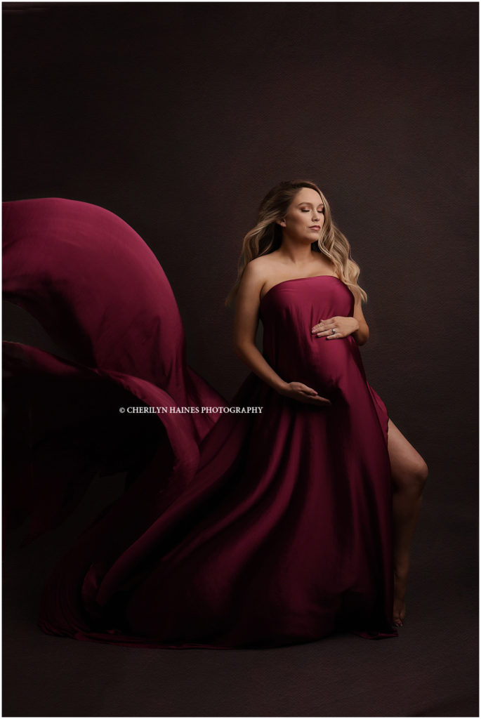 New Orleans, Louisiana fine art maternity portrait session with Cherilyn Haines Photography; Pregnant mama wearing dark berry colored silk chiffon fabric flowing in the wind with dramatic lighting; photographed in cherilyn's photography studio in Baton Rouge, Louisiana