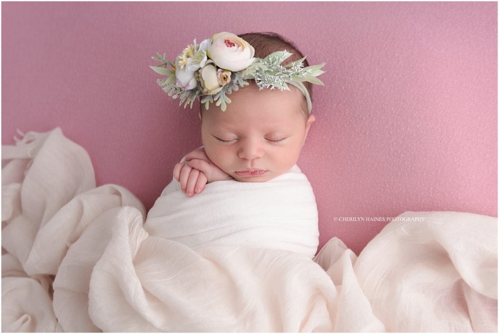 newborn girl swaddled in white wearing soft pink and green floral headband