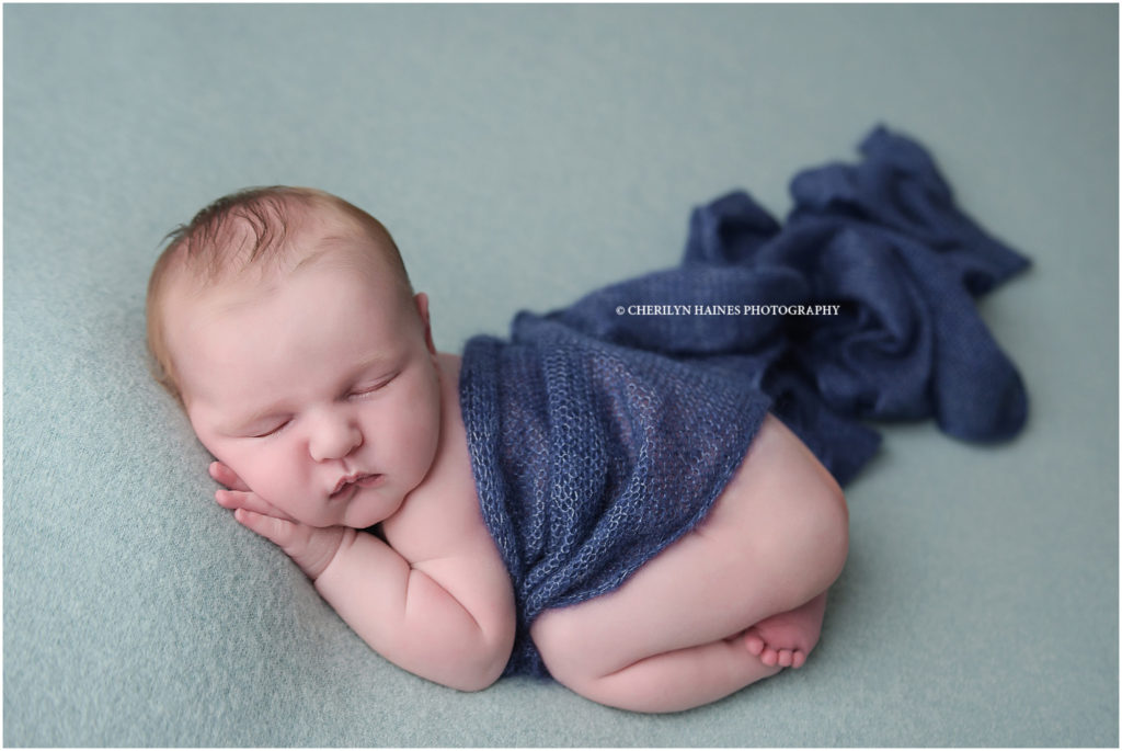 12 day old newborn baby boy is photographed by cherilyn haines photography in baton rouge, louisiana; baby boy is posed sleeping on light blue fabric with dark blue draped swaddle; cherilyn haines photograph is a fine art maternity and newborn photographer in the hammond, la area and also photographs babies in denham springs, baton rouge, new orleans, and lafayette.