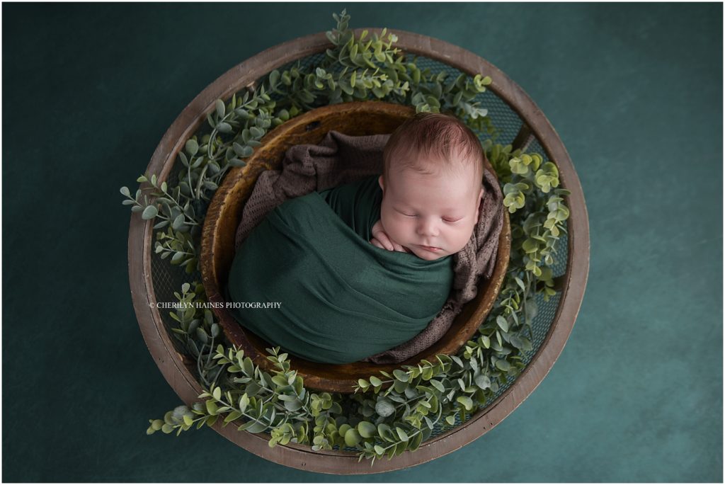 cherilyn haines photography photographed an 18 day old newborn baby boy swaddled in emerald green fabric laying in a round brown basket with greenery; cherilyn is a nikon photographer in baton rouge, louisiana