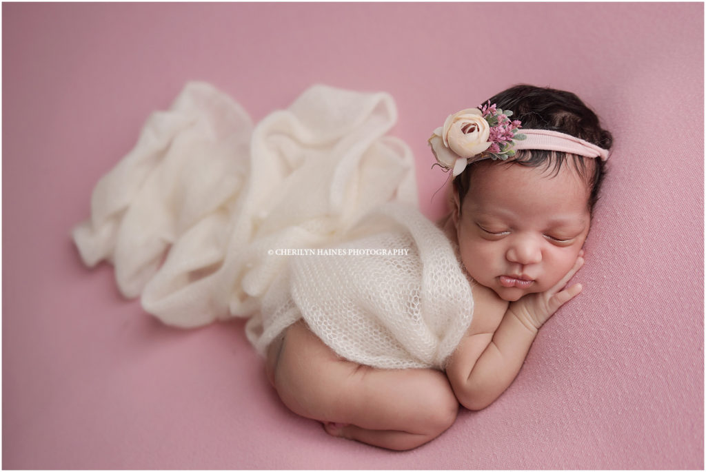 This 25 day old newborn baby girl was photographed by Cherilyn Haines Photography in her Baton Rouge, Louisiana studio. This sweet girl was born early and spent some extra time in the NICU before coming home. She slept perfectly for her newborn session while being posed on this soft pink fabric with an ivory knit wrap and coordinating floral headband.