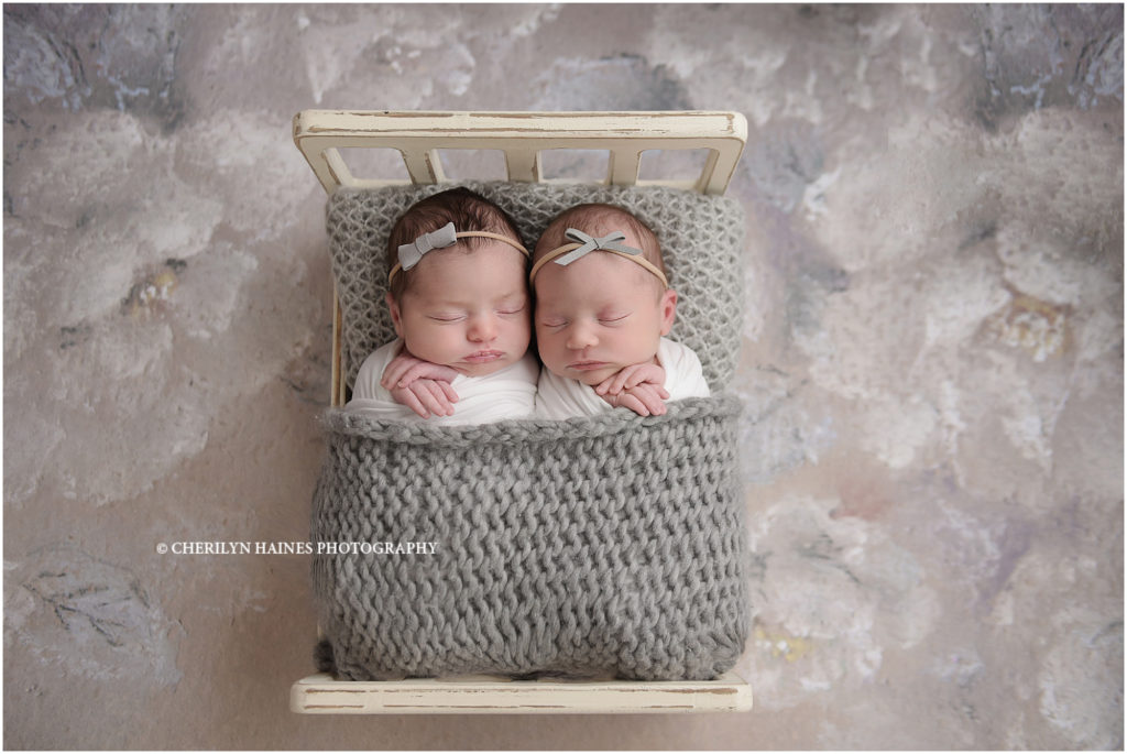 This pair of 10 day old newborn twin girls were photographed by Cherilyn Haines Photography at her Baton Rouge, Louisiana photography studio. They were swaddled in white with simple gray headbands and were photographed in a tiny wooden bed on a light gray floral backdrop.