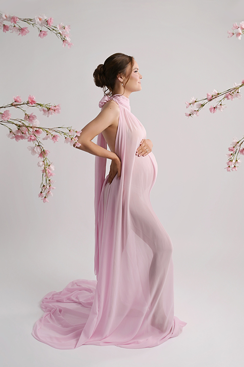 Pregnant mother wearing a soft pink maternity gown with florals in the foreground during a luxury maternity session in Baton Rouge.