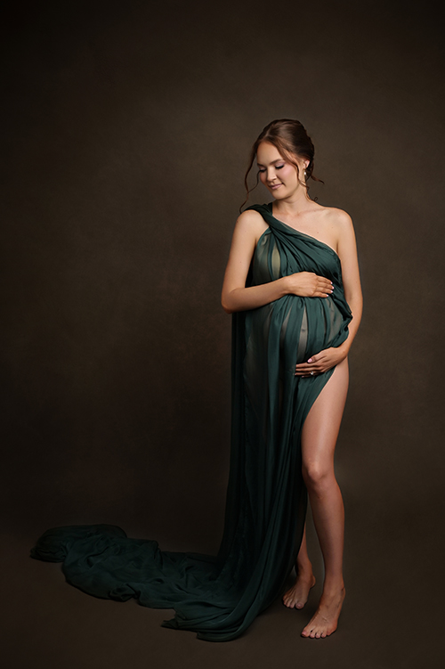 Pregnant mother wearing a deep green satin maternity gown during an elegant studio maternity session in Baton Rouge.