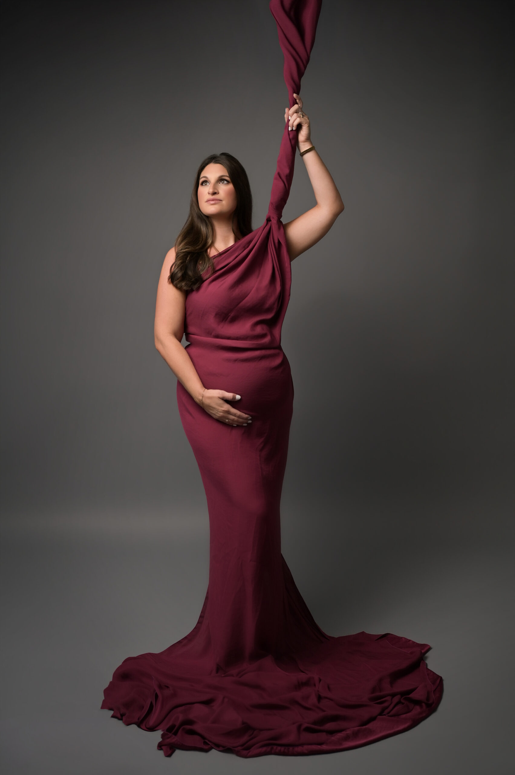 Pregnant mother wrapped in raspberry satin fabric during editorial maternity photography session in Baton Rouge