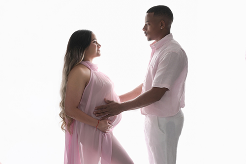 Backlit maternity portrait of an expectant couple wearing soft pink while gazing at each other during a studio maternity session in Baton Rouge.