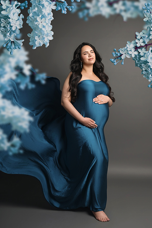 Expectant mother wearing flowing deep blue satin tossing fabric with matching blue florals during a luxury studio maternity session in Baton Rouge, Louisiana.