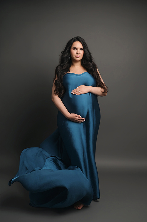 Pregnant mother posing in dramatic deep blue satin tossing fabric during a luxury studio maternity photography session in Baton Rouge.