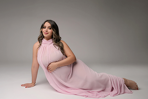 Pregnant mother sitting on the studio floor wearing a flowing pink maternity gown during her Baton Rouge maternity photography session.
