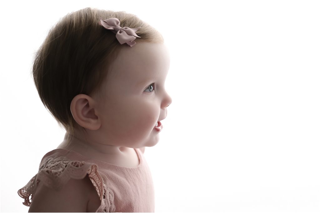 Smiling 6 month old baby girl photographed in a softly backlit profile portrait