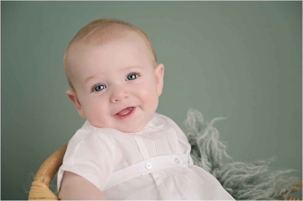 6 month old baby boy smiling while posed in a basket on a sage green backdrop during a Baton Rouge baby photography session