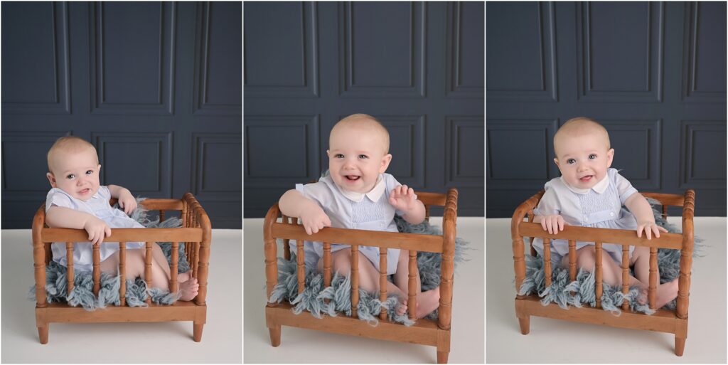 6 month old baby boy sitting in a brown wooden crib against a navy wainscoting backdrop during a Baton Rouge baby photography session