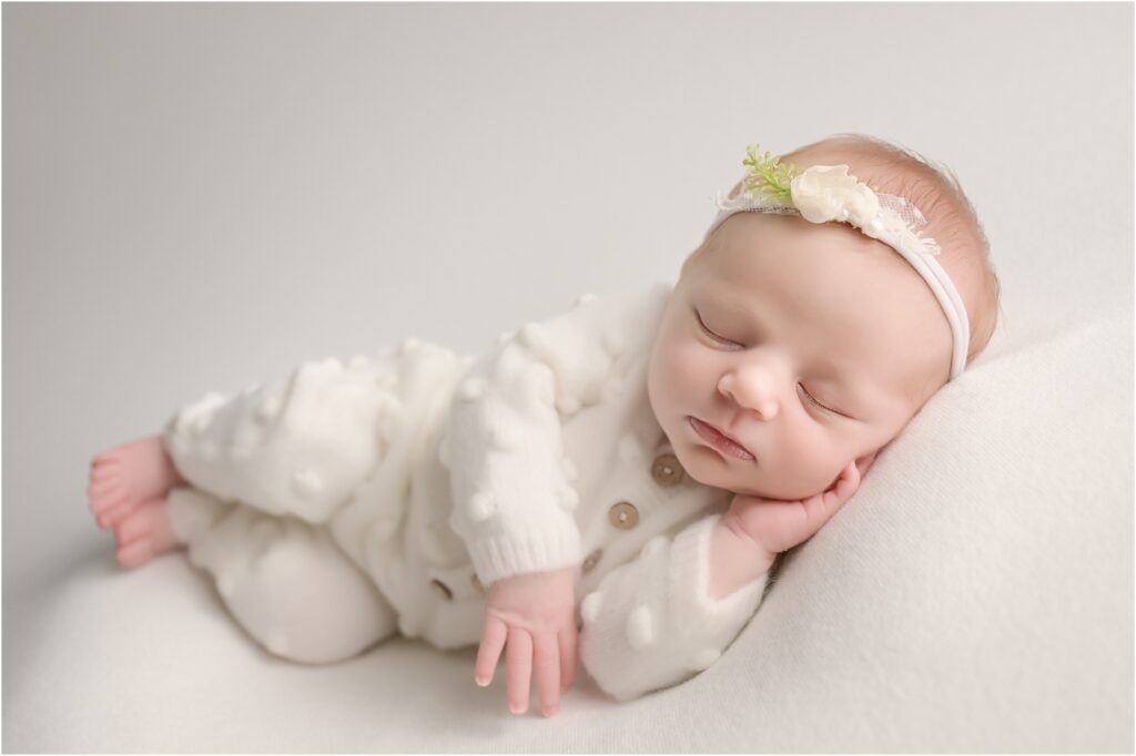 Newborn baby girl peacefully posed on her side wearing a white romper